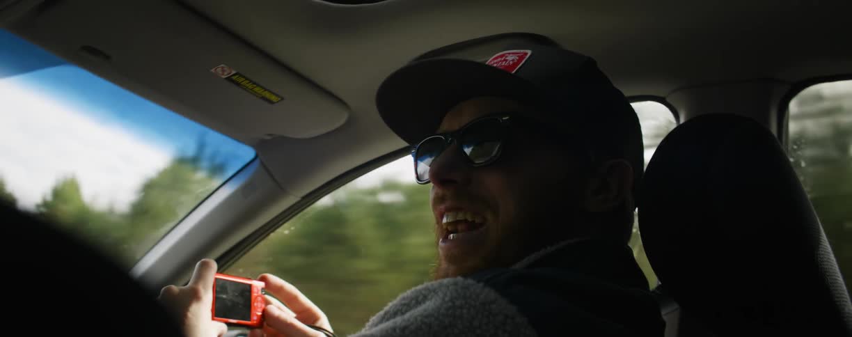 A passenger in a vehicle uses a compact camera and laughs