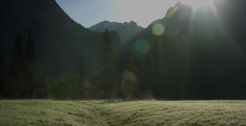 The sun casts bright light into a field in a mountain valley