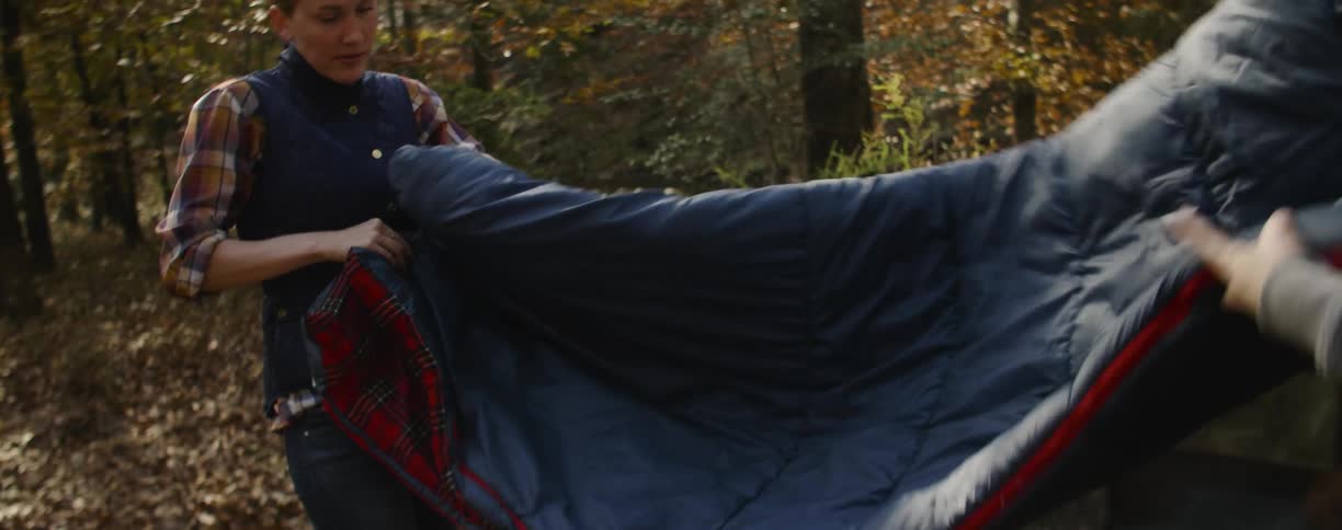Two campers fold up a sleeping bag in the woods