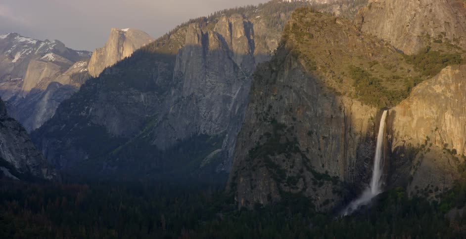 The sun shines on a waterfall in a mountain range