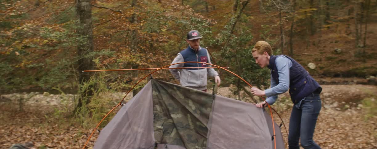 Man and woman set up a tent in the middle of the forest