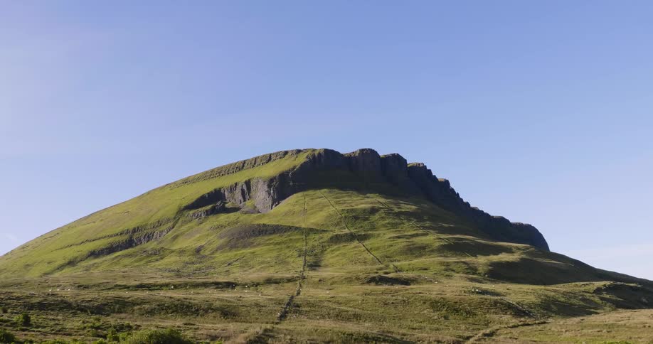 The small mountain is covered with grass and the sky is clear