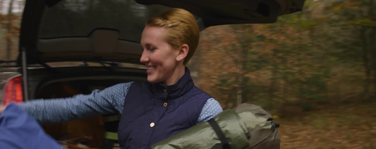 Smiling man and woman unpack a ca trunk in the woods