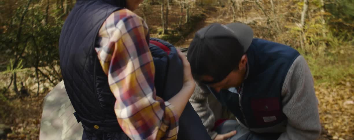 Man and woman roll up a sleeping bag together in the woods
