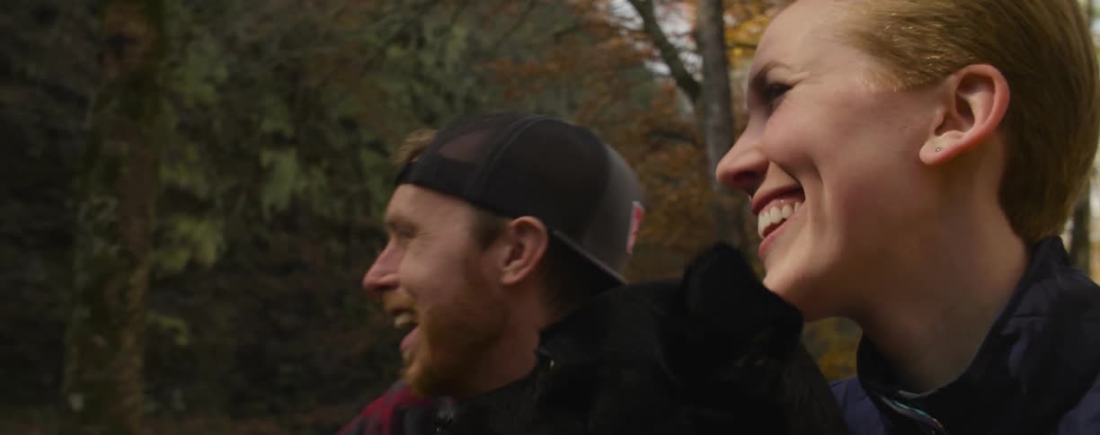 Couple laughing outdoors with their dog in the fall