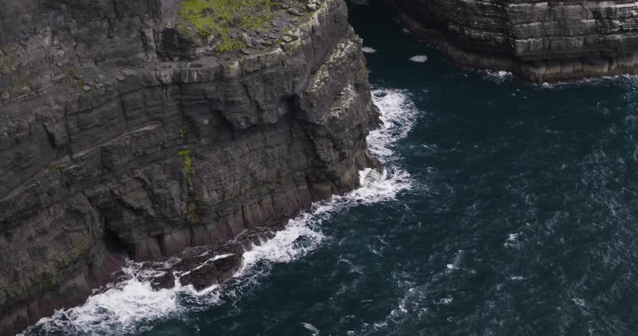 Waves crash against the base of cliffs during the day