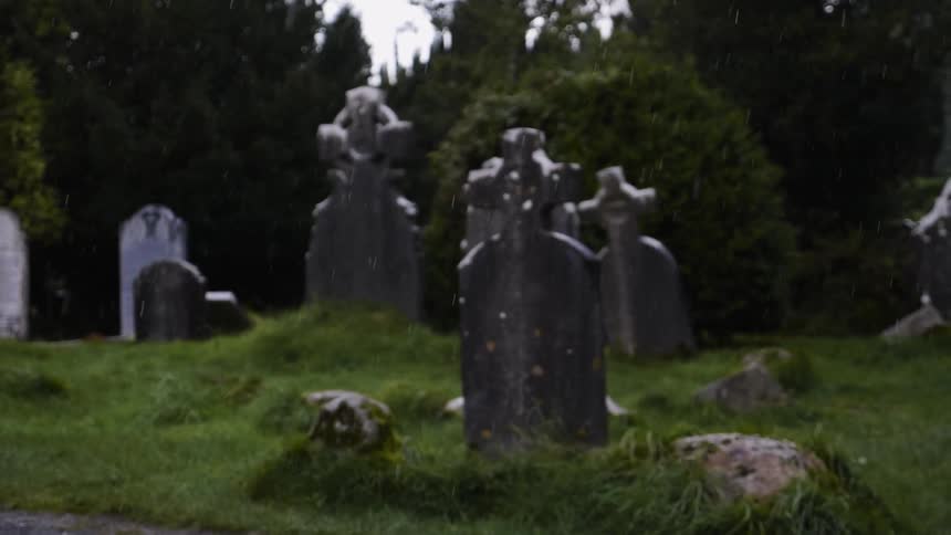 Rain falls around old tombstones in a cemetery
