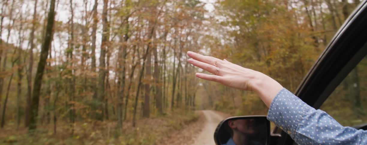 A woman holds her hand out of a vehicle window and plays with the air