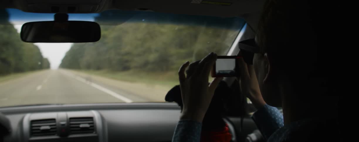 A woman rides in a car with a dog on her lap and takes a picture