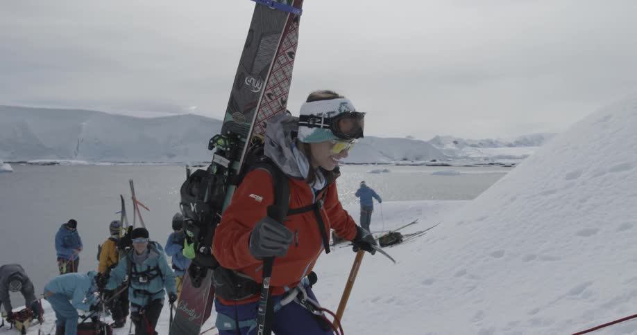 An excited woman carrying a backpack and skis cheers as she starts out on a trek