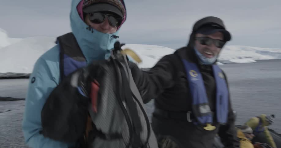 Backpacks are passed from a boat to the shore in a line of people