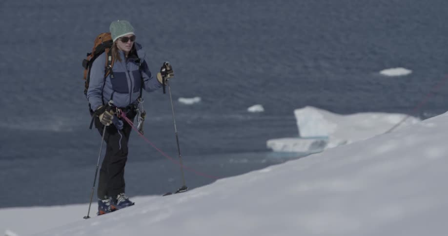 A woman walking uphill in the snow with skis and poles (medium)