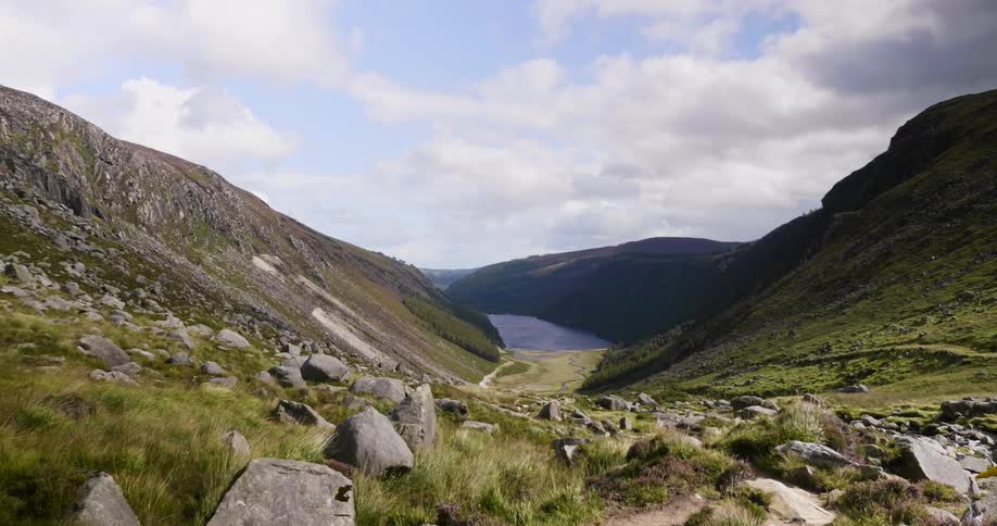 The wind rustles the grass in a valley leading to a fjord on a cloudy day