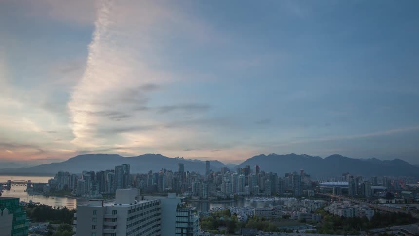 A wide view of a large city with tall buildings near a body of water, as the day turns into dusk