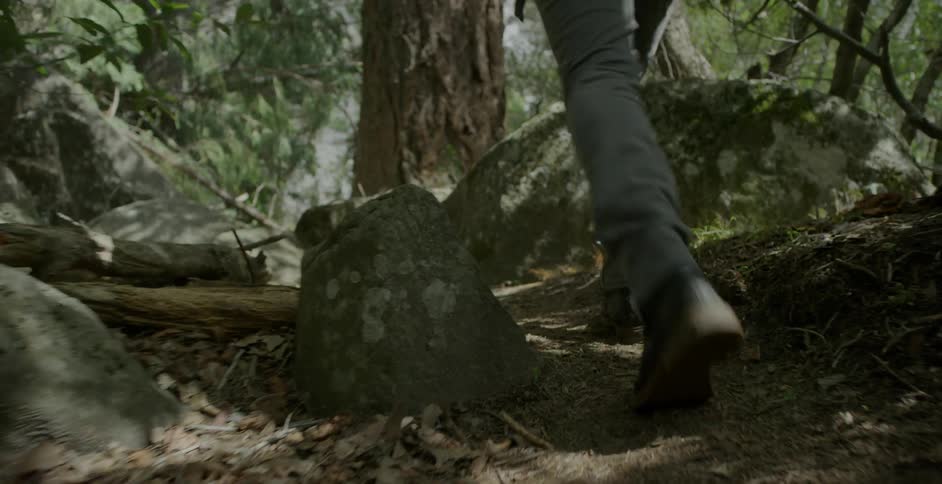 A man hikes across rocky ground in the woods
