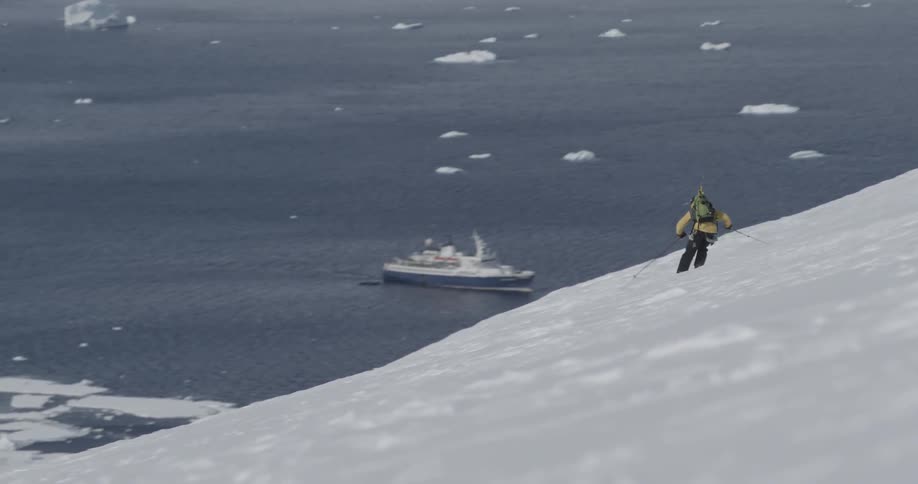 A man skis down a hill toward a body of water with ocean behind