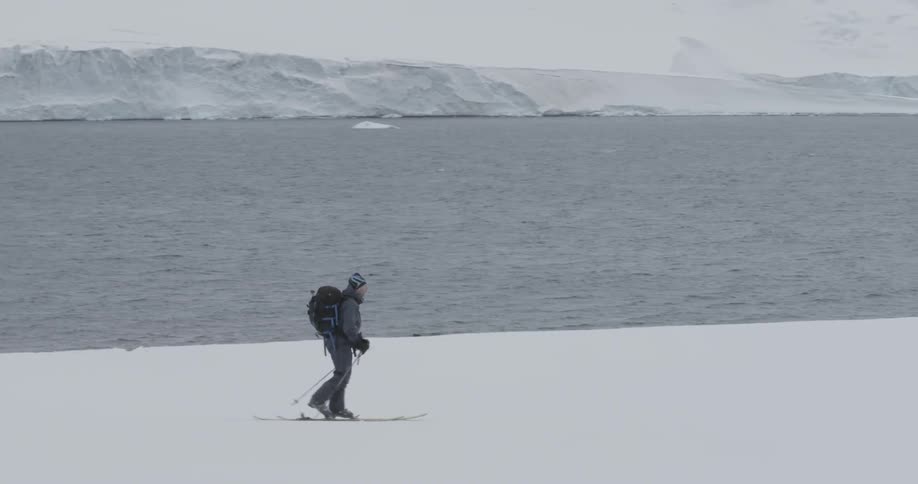 A man skinning / skis near the water with  snowy jagged coast in the background