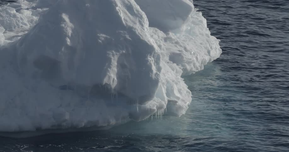 A large iceberg floats in the water with icicles