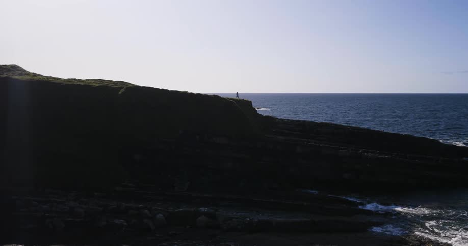 A person standing on a large rock that leads out into the water