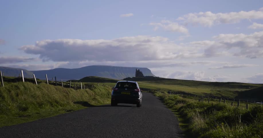 A car traveling down a country road surrounded by green fields
