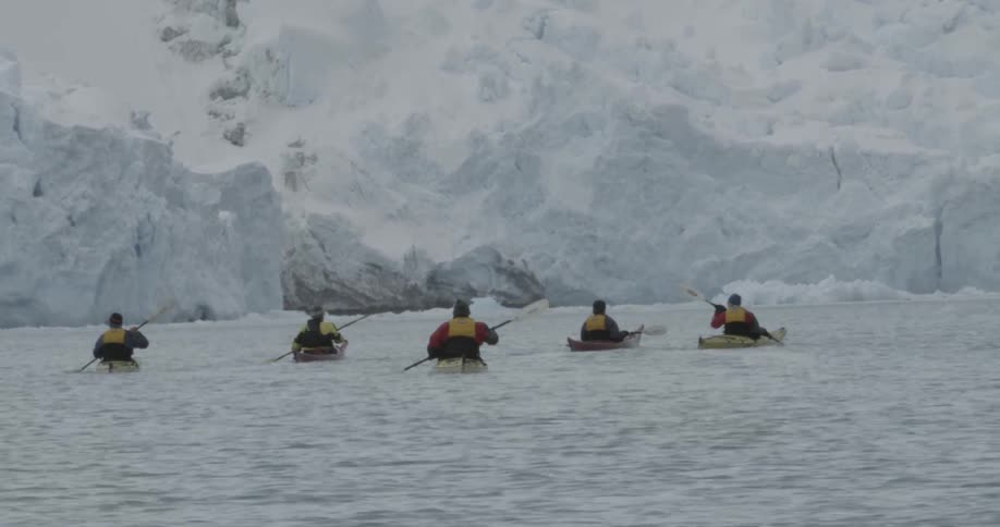 A group of people kayaking near a big glacier with ice shelf
