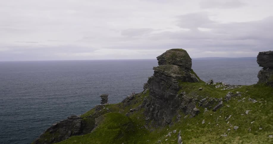 Two people stand on the ridge of a cliff overlooking the ocean on a cloudy day