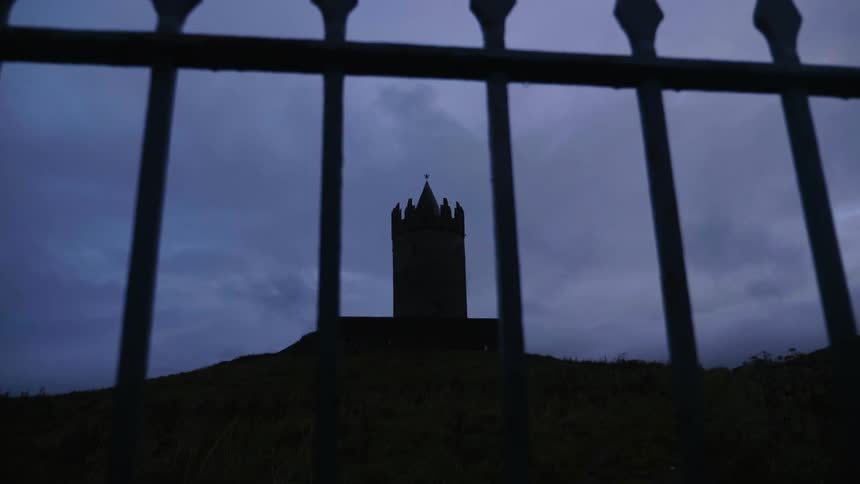 A view of a fence that is enclosing a castle on a big hill