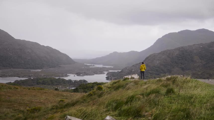 Person standing on a grassy hill looks out at a river and hills