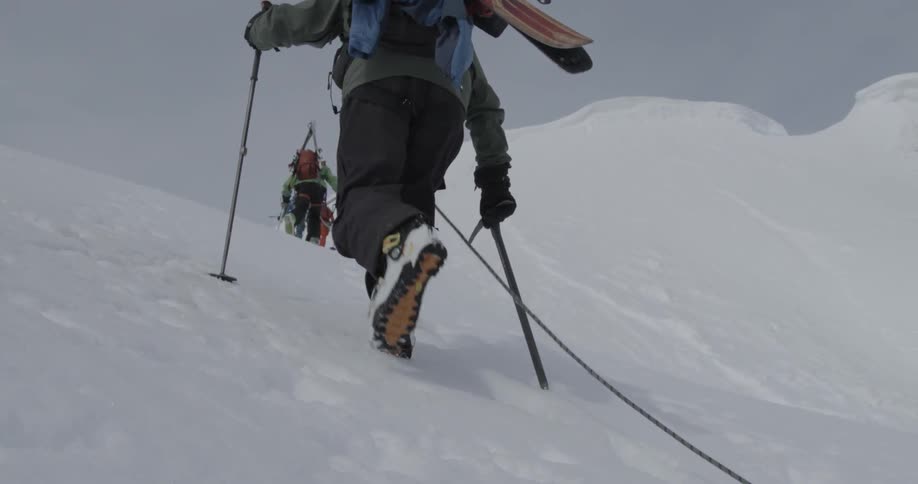People using poles and ice axe to hike up snow covered slope