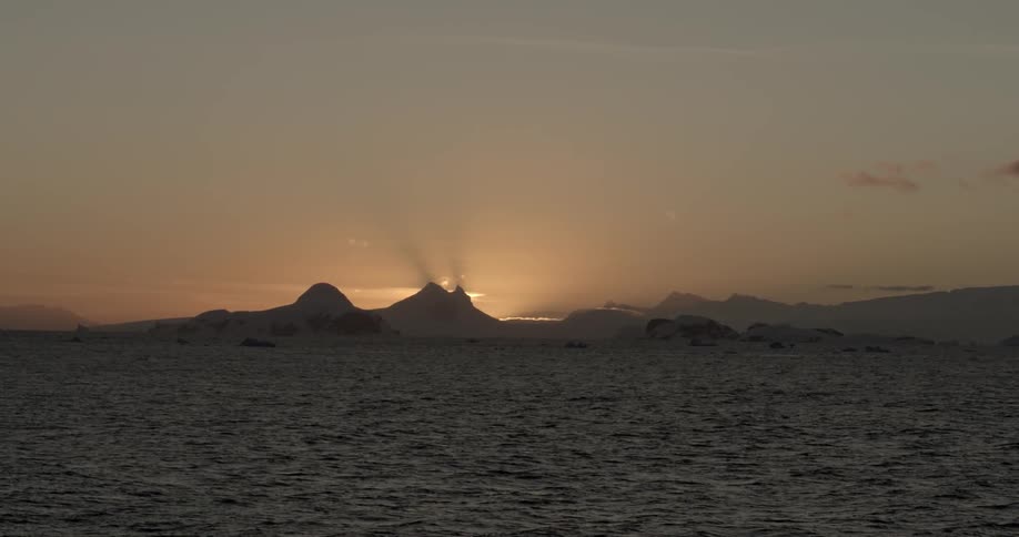 The warm sun is setting beyond a cold glacier at the ocean