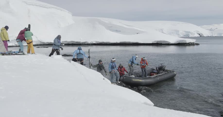 Group of people unloading a raft onto a snowy shore (wide angle)