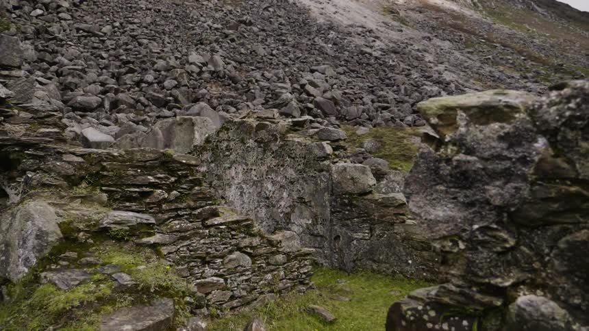 Moss grows on a crumbling rock wall at the base of a mountain slope