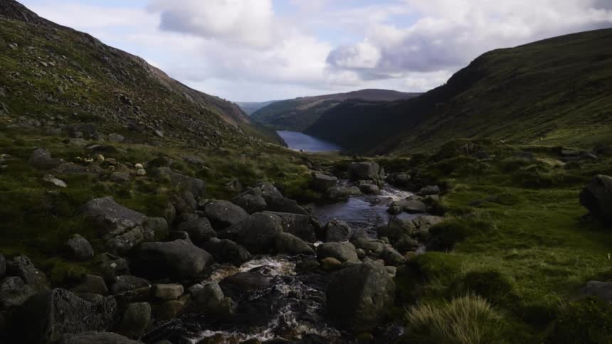 A creek runs over rocks toward a river in a mountain valley