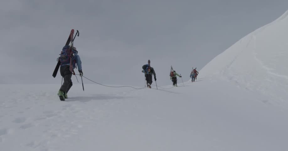 A group of skiers hike up a snow covered mountain while tied together with a safety rope