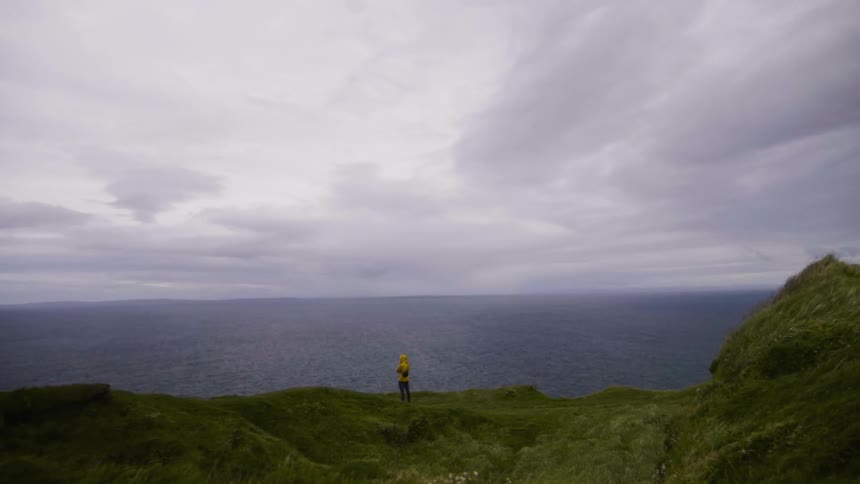 A person stand on a cliff overlooking the ocean watching the view
