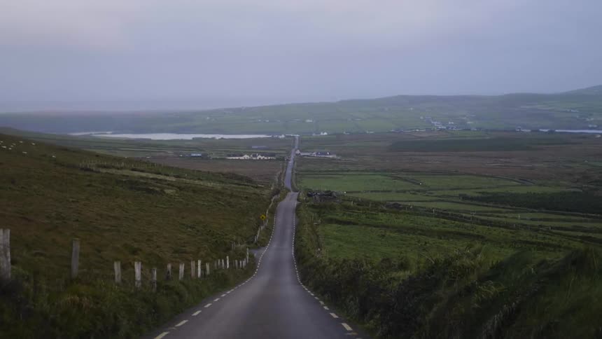 A narrow road runs towards a shoreline in a valley on an overcast day