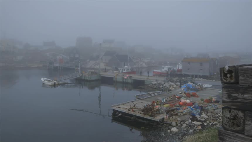 Boat sits in the lake next to a dock covered with trash under a foggy sky