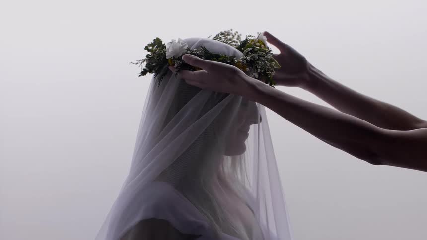 A floral wreath is placed on the head of a woman wearing a white veil