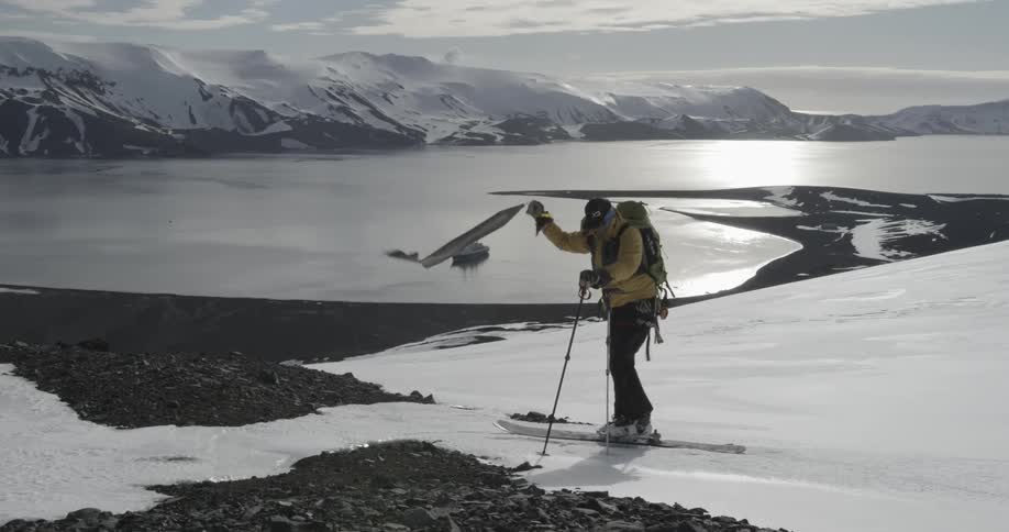 Man takes skins off of skis to prepare for descent down crater with large bay behind