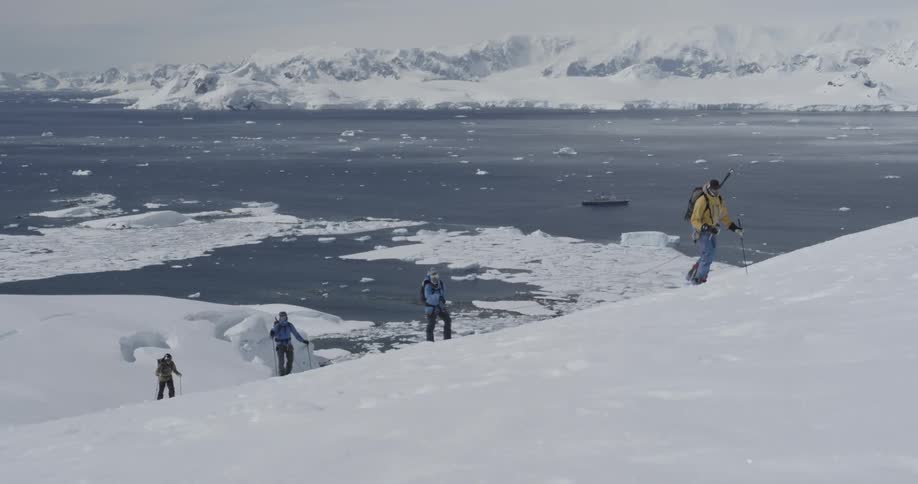 Four people tied together climb a snow covered slope icebergs and icy water behind