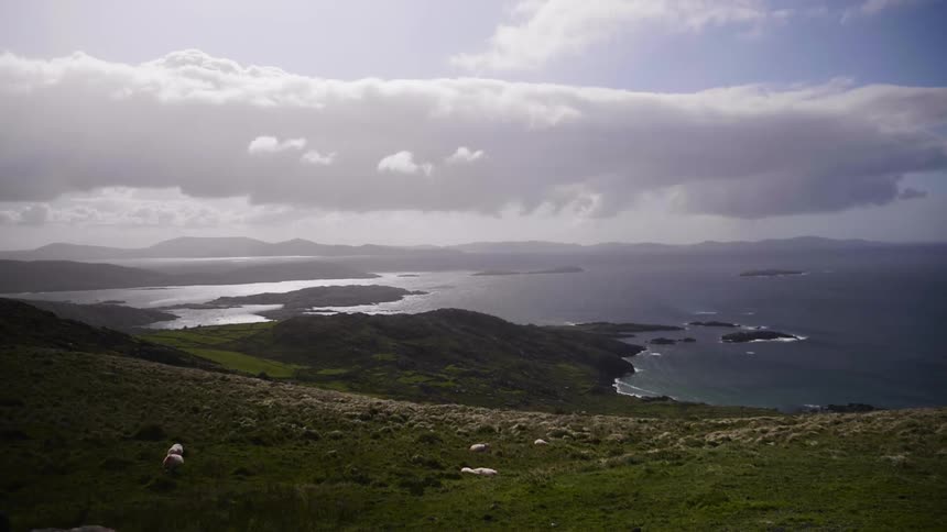 Clouds hang over a coastline as horses graze on the hillside