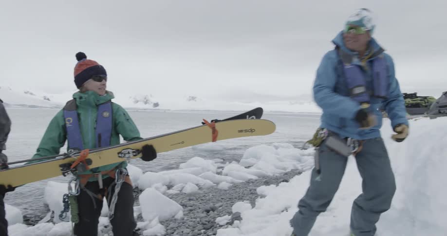 People hand skis from person to person out of boat to shore