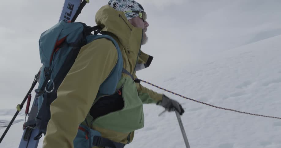 Man carrying skis trudges up a hill in a line with other skiers