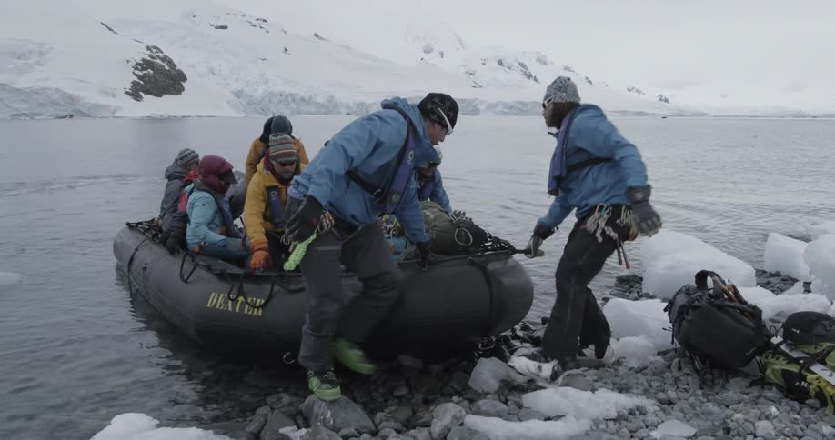Group of explorers climb off a raft onto a snowy rocky shore