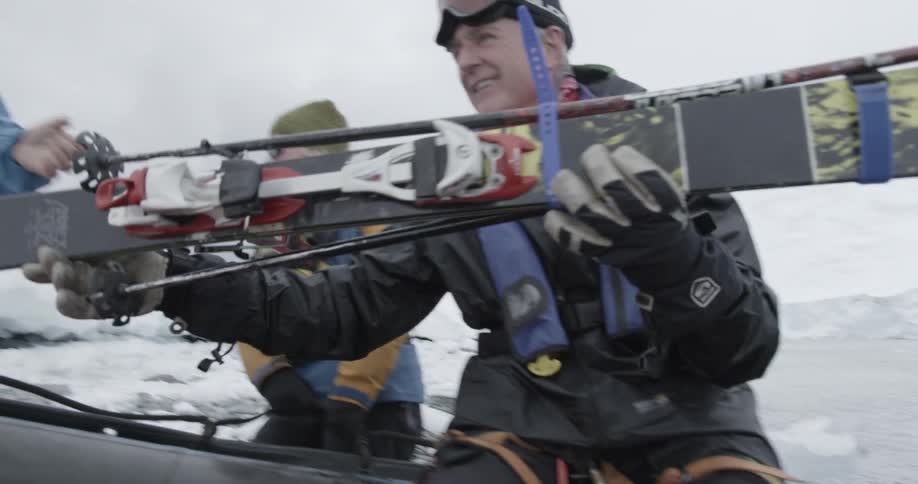 People unload skis off of a zodiac onto shore