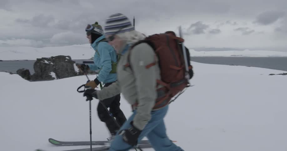 Two women pass by walking while wearing skis in a snowy landscape