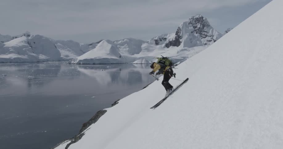 Professional skier turns down a steep slope to water below (slow motion)