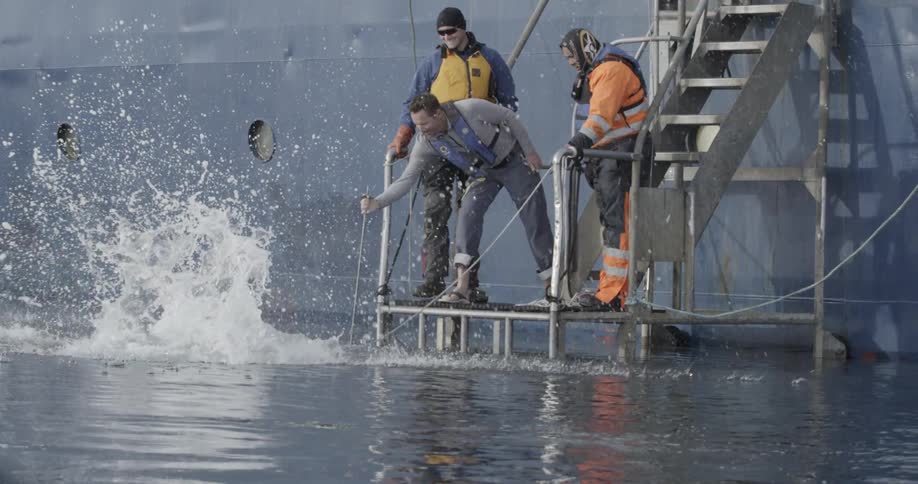 A man does a slow motion backflip off a ship's platform into the water