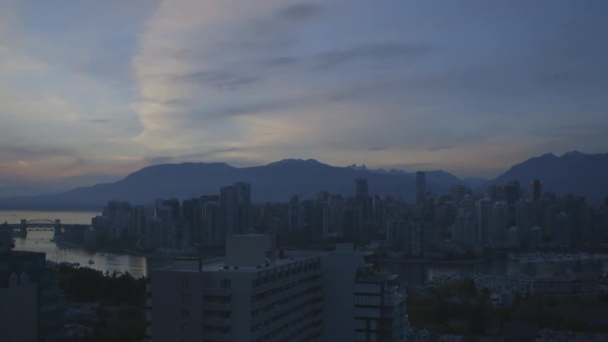 Aerial view of a city, the ocean and mountains under a cloudy sky at dusk