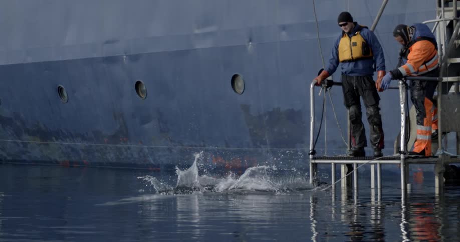 A man jumps from a platform into freezing cold water as two men watch over him